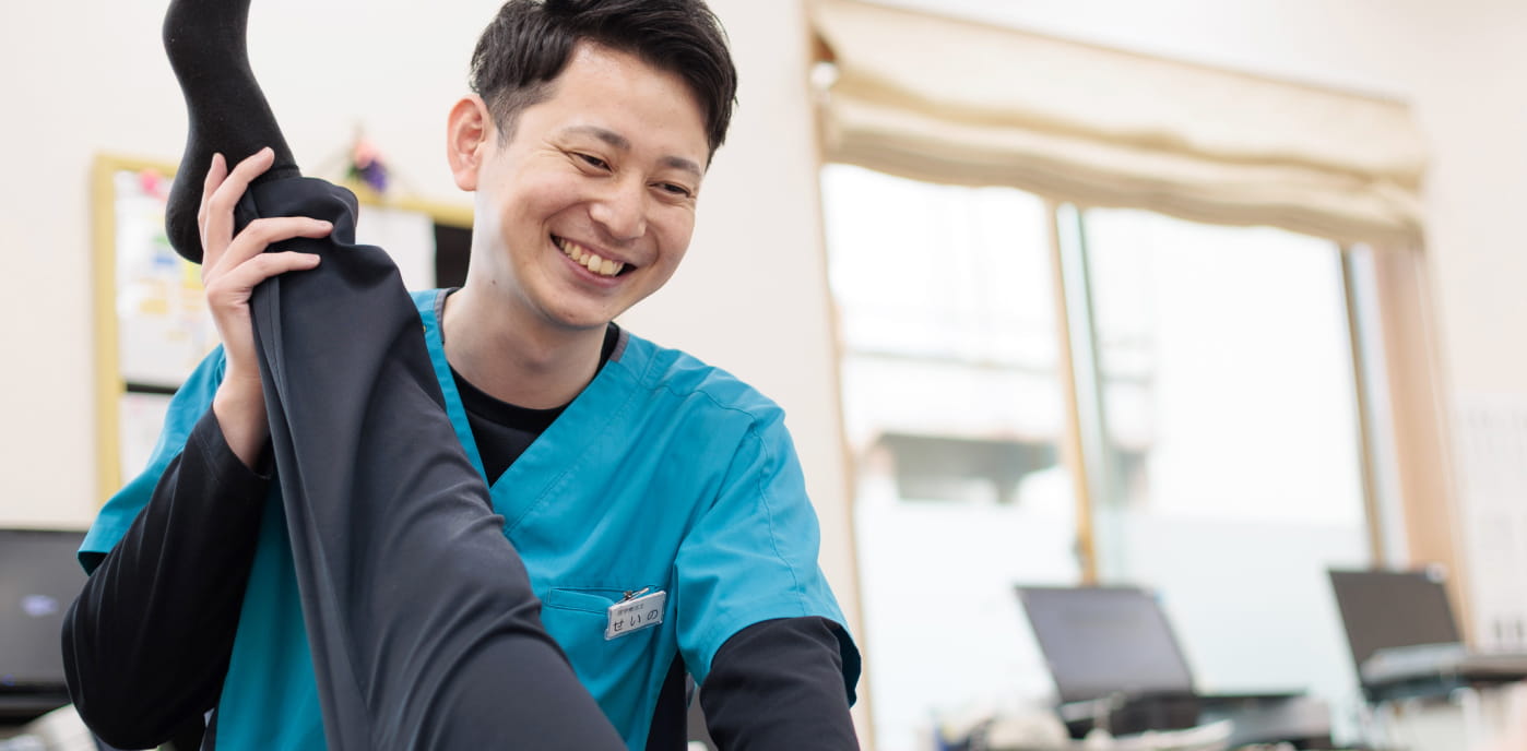 笑顔の男性看護師が患者の足をストレッチしている